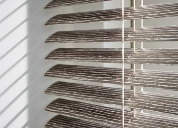 Luxaflex Venetian blinds made from wood, shown partially opened and casting a shadow on the adjacent wall