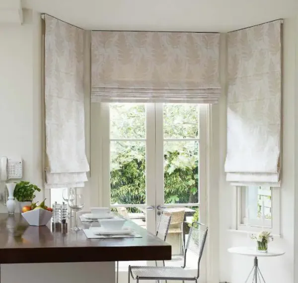 A kitchen island and barstools decorated in neutral colours against double doors and windows fitted with cream roman blinds in Stowmarket