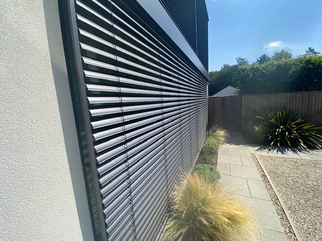 Side view of external venetian blinds with adjustable horizontal slats fitted beside a landscaped walkway